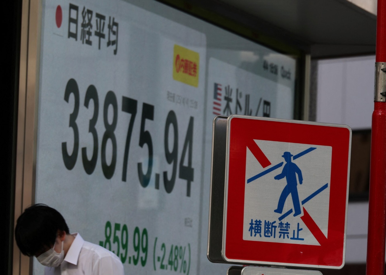 日本东京，一名男子走过一家经纪公司外显示日经平均指数的股票报价板